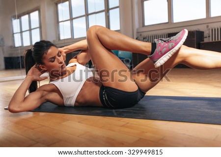 Young fit woman exercising in a gym lying on mat doing leg raising and twisting exercises. Young attractive woman doing abs workout. Fitness woman doing a sit up.