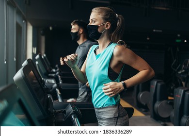 Young fit woman and man running on treadmill in modern fitness gym. They keeping distance and wearing protective face masks. Coronavirus world pandemic and sport theme. - Powered by Shutterstock