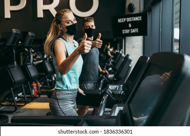 Young fit woman and man running on treadmill in modern fitness gym. They keeping distance and wearing protective face masks. Coronavirus world pandemic and sport theme. - Powered by Shutterstock