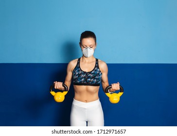 Young Fit Woman With N96 Face Mask  Doing Biceps Exersice At The Gym With Kettlebells. Fitness Strength Workout Under Coronavirus Health Crisis.