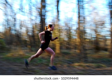 Young, Fit Woman With Ponytail Wearing Black Fitness Clothes Running Through Woods On A Sunny Afternoon In Winter, Cross Country Triathlete (motion Blurred Image)