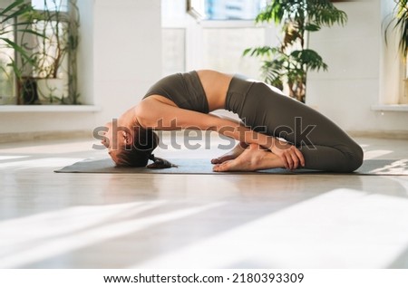 Young fit woman practice yoga doing asana in light yoga studio with green house plant