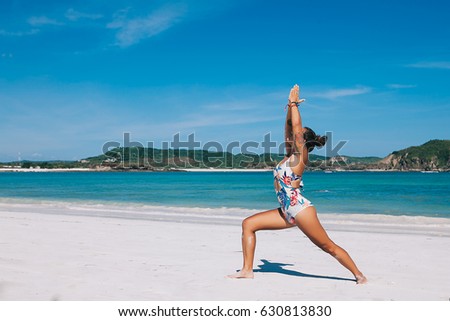 Young fit woman practicing yoga and meditation outdoor on white sand beach during vacation retreat in Bali, blue ocean background