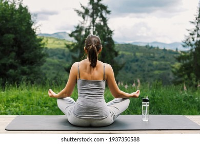 Young fit woman practising meditation on yoga mat on background of sunny mountains hills. Outdoor workout and training. Healthy lifestyle. Sporty Female doing yoga on wooden terrace among trees
