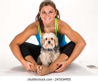 Young fit woman relaxing with dog after workout listening to music on earbuds.
