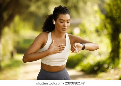 Young fit woman runner in sportswear checking smartwatch for heart rate, pausing and breathing in run, focused on health and training outdoors in park. Wellbeing and exercise concept - Powered by Shutterstock