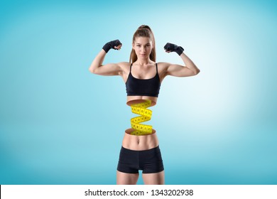 Young Fit Woman In Short Black Gym Top And Shorts, In Double Bicep Pose, Upper Body Cut At Waist And Measuring Tape Connecting Two Parts Of Woman. Watch Weight. Keep Fit. Stay Young And Healthy.