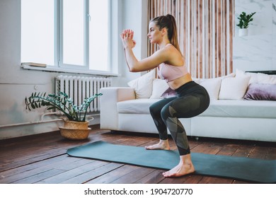 Young Fit Woman In Sportswear Do Squat Exercise Indoors In Living Room. Online Indoors Workout. Training At Home