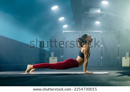 Young fit woman in sportswear doing yoga at gym in upward facing dog pose.