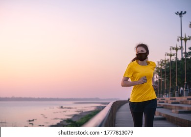 Young Fitness Asian Woman Running And Exercise With Wearing A Protective Mask COVID-19 An Outdoor Workout On The Riverwalk In The Morning.