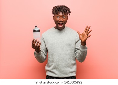 Young fitness black man holding a water bottle celebrating a victory or success