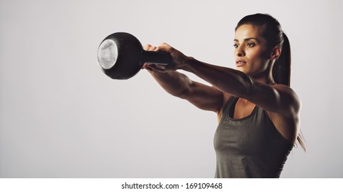 Young fitness female exercise with kettle bell. Mixed race woman doing crossfit workout on grey background. Kettlebell swing. - Powered by Shutterstock