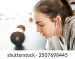 Young fitness girl with sweat on face feeling exhausted after hard workout in gym, sitting and listening music, breathing exercise.