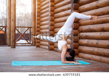 Young fitness indian woman practicing yoga on wooden terrace in the background. Wellness concept. Handstand pose