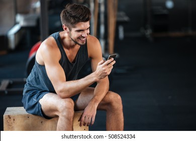 Young Fitness Man Sits On The Box And Looking At The Phone