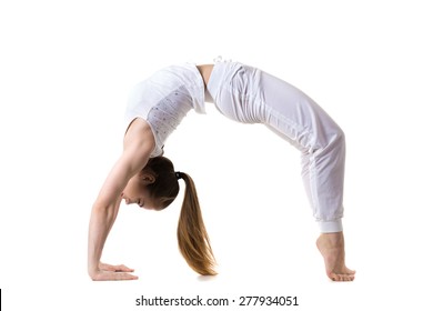 Young fitness model in white sportswear doing yoga or pilates training, exercise bridge, urdhva dhanurasana, Upward Bow (Wheel) yoga Pose, side view