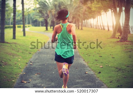 Young fitness sportswoman runner running on tropical park trail