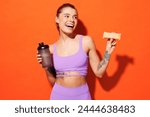 Young fitness trainer instructor sporty woman sportsman wear purple top clothes in home gym eat protein bar hold cocktail look aside isolated on plain orange background Workout sport fit abs concept