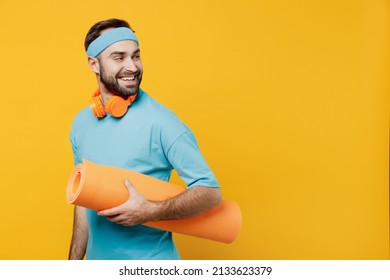 Young fitness trainer instructor sporty man sportsman in headband blue t-shirt spend weekend in home gym hold yoga mat look aside isolated on plain yellow background. Workout sport motivation concept - Powered by Shutterstock