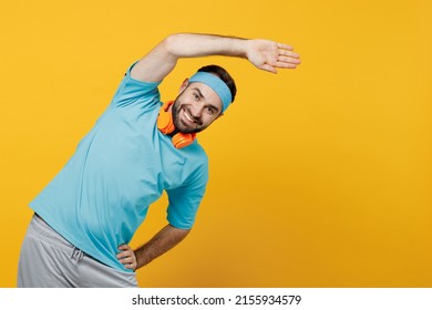 Young Fitness Trainer Instructor Sporty Man Sportsman In Headband Blue T-shirt Tilt Body To Sides With Hand, Stretch Lunge Exercise Isolated On Plain Yellow Background Workout Sport Motivation Concept