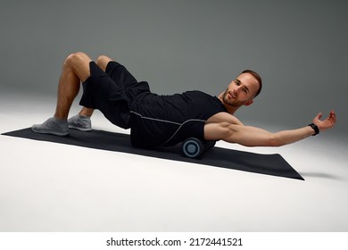 Young Fitness Trainer Instructor Sporty Man Sportsman On Foam Roll And Yoga Mat Isolated On Gray Background. Workout Sport Motivation Concept.