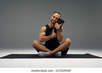 Young Fitness Trainer Instructor Sporty Man Sportsman Hold Foam Roll Sitting On Yoga Mat Isolated On Gray Background. Workout Sport Motivation Concept.