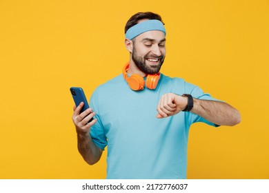 Young fitness trainer instructor sporty man sportsman in headband blue t-shirt spend weekend in home gym using smart watch mobile cell phone isolated on plain yellow background. Workout sport concept