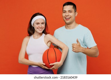 Young Fitness Trainer Instructor Sporty Two Man Woman In Headband T-shirt Hold Ball Play Basketball Show Thumb Up Spend Weekend In Home Gym Isolated On Plain Orange Background. Workout Sport Concept