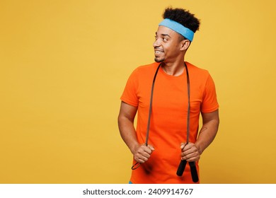 Young fitness trainer instructor sporty man sportsman wears orange t-shirt hold skipping rope look aside area spend time in home gym isolated on plain yellow background. Workout sport fit abs concept - Powered by Shutterstock