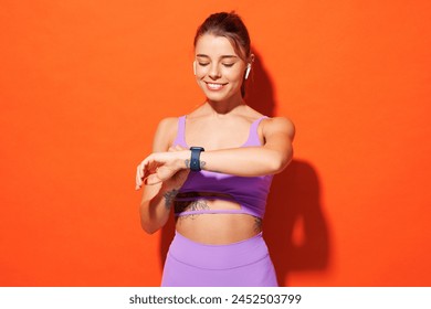 Young fitness trainer instructor woman sportsman wears purple top clothes smartwatch spend time in home gym listen music in earphones isolated on plain orange background. Workout sport fit abs concept - Powered by Shutterstock