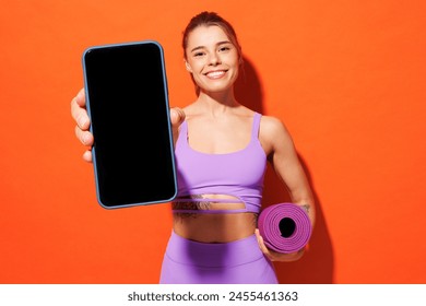 Young fitness trainer sporty woman sportsman wears purple top clothes in home gym hold yoga mat use blank screen mobile cell phone isolated on plain orange background. Workout sport fit abs concept - Powered by Shutterstock