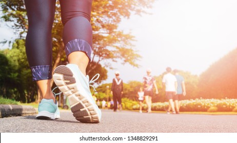 Young Fitness Woman Legs Walking With Group Of People Exercise Walking In The City Public Park In Morning.