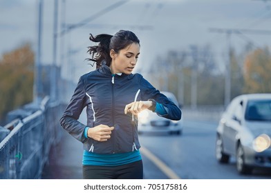 Young fitness woman runner checking time from smart watch. Young woman checking heart rate while jogging on street at dusk. Young woman looking on smartwatch her heartbeat while running in city. 
 - Powered by Shutterstock