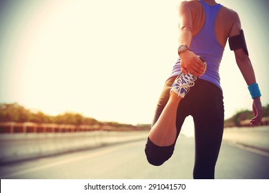 Young fitness woman runner stretching legs before run on city