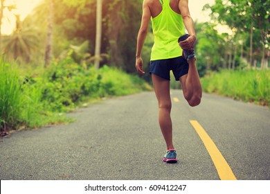 Young Fitness Woman Runner Stretching Legs Before Running At Morning Tropical Forest Trail 