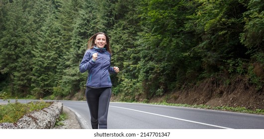 Young fitness woman running on the road through the forest. Slim girl jogging in the morning along the road. - Shutterstock ID 2147701347