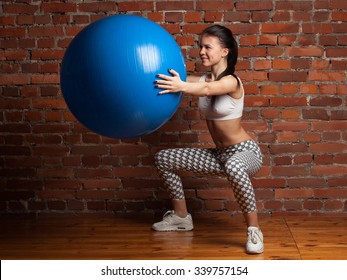 Young Fitness Woman Squat With Fitball In Hand, Against Brick Wall 