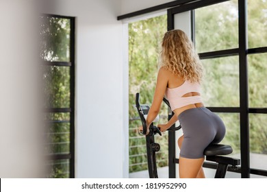 Young Fitness Woman Use Exercise Bike And Training Hard At Home Gym Near Window With Nature View. Sporty Lifestyle