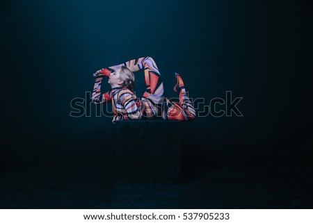 Young flexible blonde circus acrobat posing in studio in costume. Doing equilibre balance handstand on a cube. Copy space text.