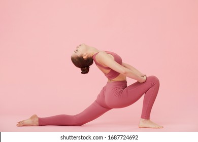 Young flexible woman doing stretching exercise over pink background