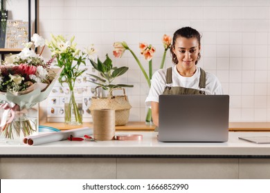 Young Flower Shop Owner Using Laptop At Counter. Woman Florist Standing At Table. 