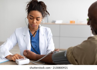 Young Focused African American Lady Examining Older Patient Measuring Arterial Blood Pressure With Stethoscope And Sphygmomanometer Medical Device Sitting At Table. Hypertension Health Problem Concept