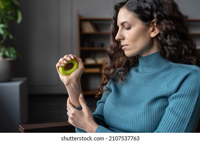 Young Focused Female Office Worker Exercising With Hand Grip At Workplace, Strengthening Wrist And Forearm, Woman Employee Doing Squeeze-and-release Exercises With Carpal Expander, Selective Focus