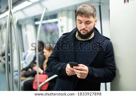 Young focused man browsing and typing messages on phone on way to work in modern metro car