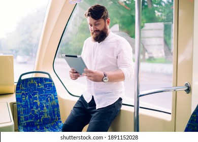 Young Focused Man In Casual Clothes And Wristwatch Leaning On Window In Modern Train While Browsing Web In Soft Daylight