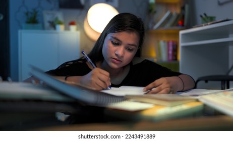 Young focused school, college girl with pen in hand write, study, think, doing assignment project homework for exams. Hard working Indian teen concentrating, read alone late hours in night at home  - Shutterstock ID 2243491889