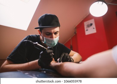 Young Focused Tattoo Artist Is Inking Customers Arm Carefully In His Shop.