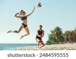 Young focused woman in sunglasses hitting ball, while man staying focused. Young people, friends playing beach volleyball. Concept of sport, summer, nature, active lifestyle, youth