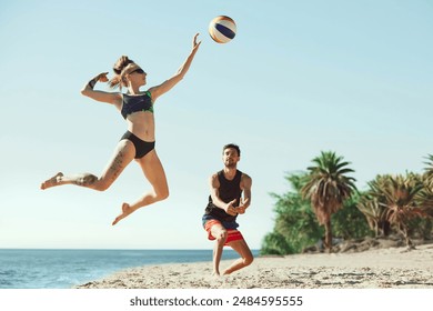 Young focused woman in sunglasses hitting ball, while man staying focused. Young people, friends playing beach volleyball. Concept of sport, summer, nature, active lifestyle, youth - Powered by Shutterstock