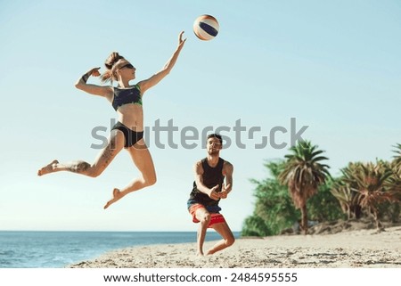 Young focused woman in sunglasses hitting ball, while man staying focused. Young people, friends playing beach volleyball. Concept of sport, summer, nature, active lifestyle, youth